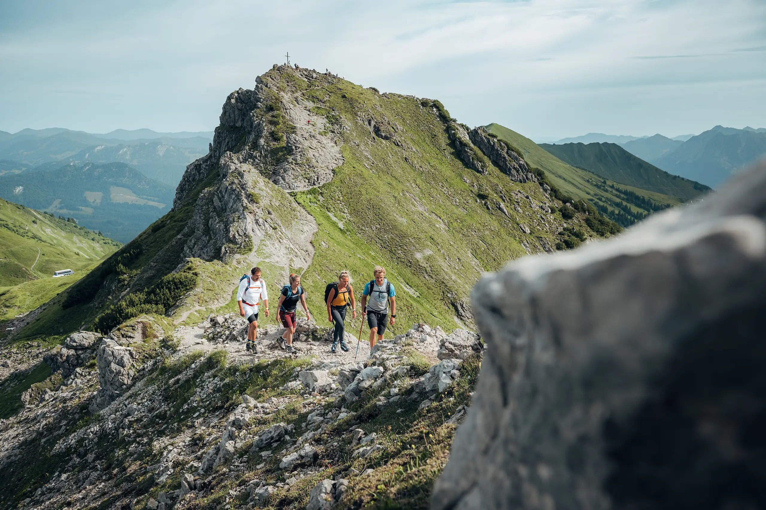 Vier Wanderer auf einem schmalen Bergpfad im Kleinwalsertal mit Blick auf Gipfel und Gipfelkreuz