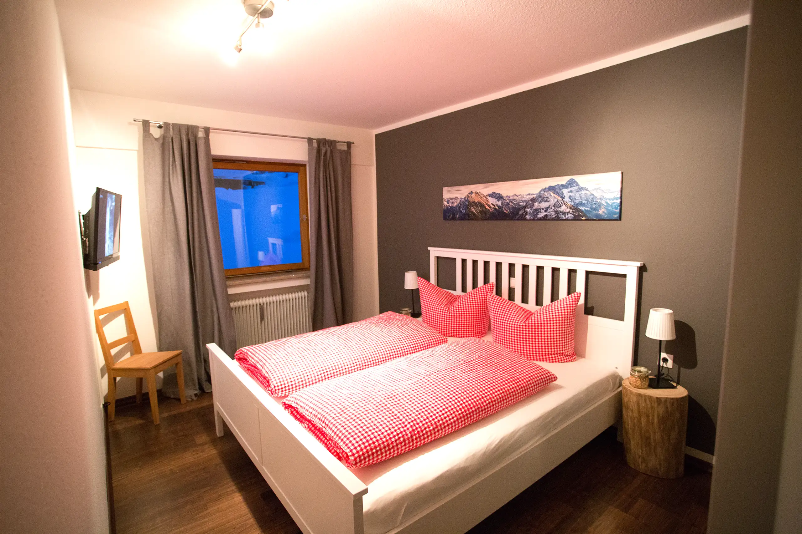 Schlafzimmer der Ferienwohnung Ifenblick mit Doppelbett, rot-karierter Bettwäsche und Bergbild
