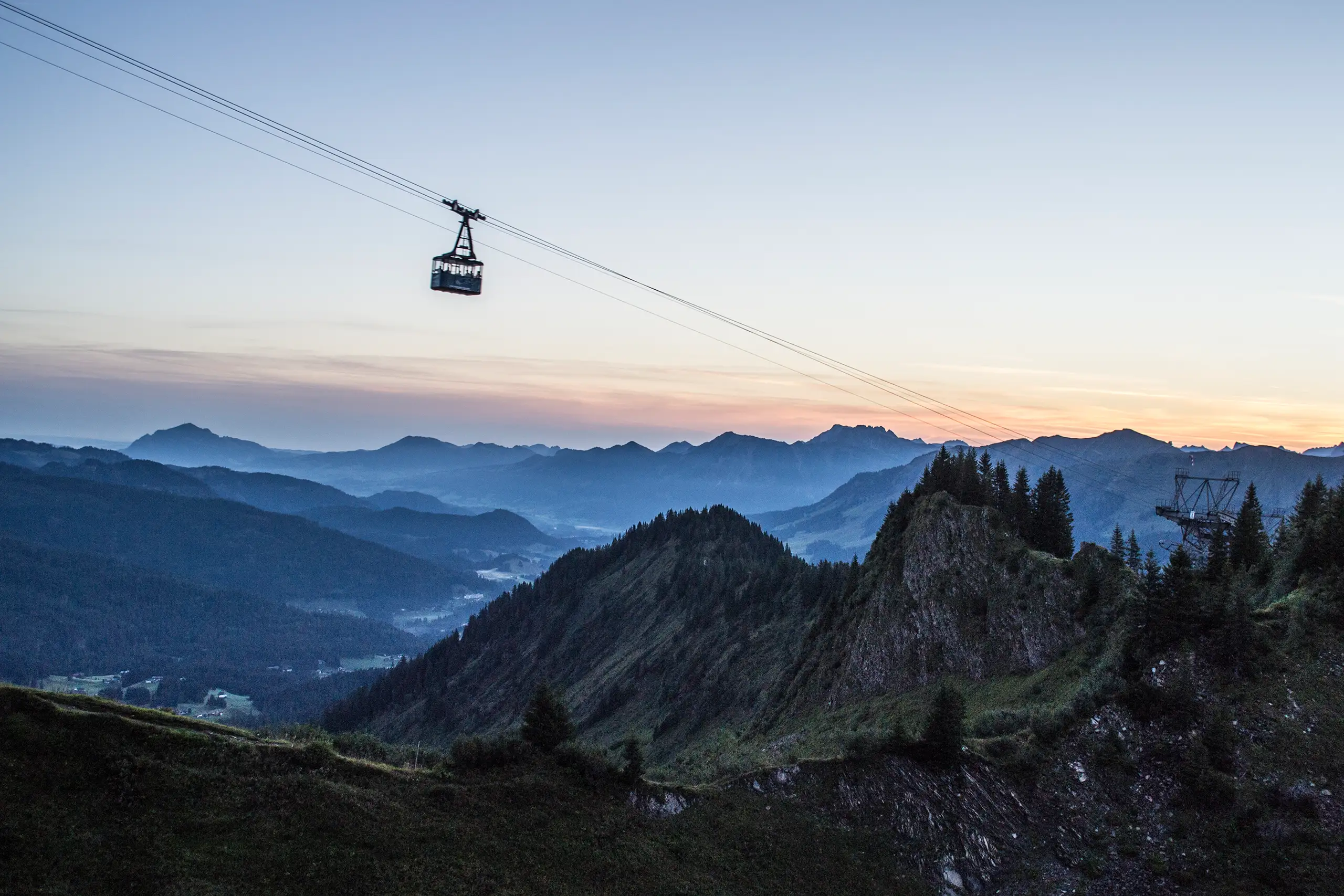 Seilbahn-Gondel über bewaldeter Berglandschaft im Kleinwalsertal bei Sonnenuntergang