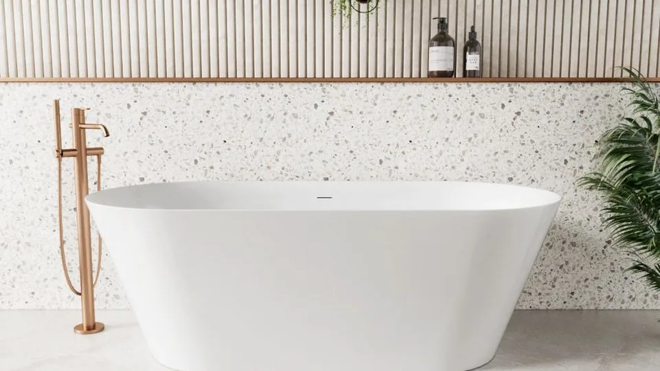 Alpine oval freestanding bath with a floor mounted bath filler beside it, against a terrazzo look wall
