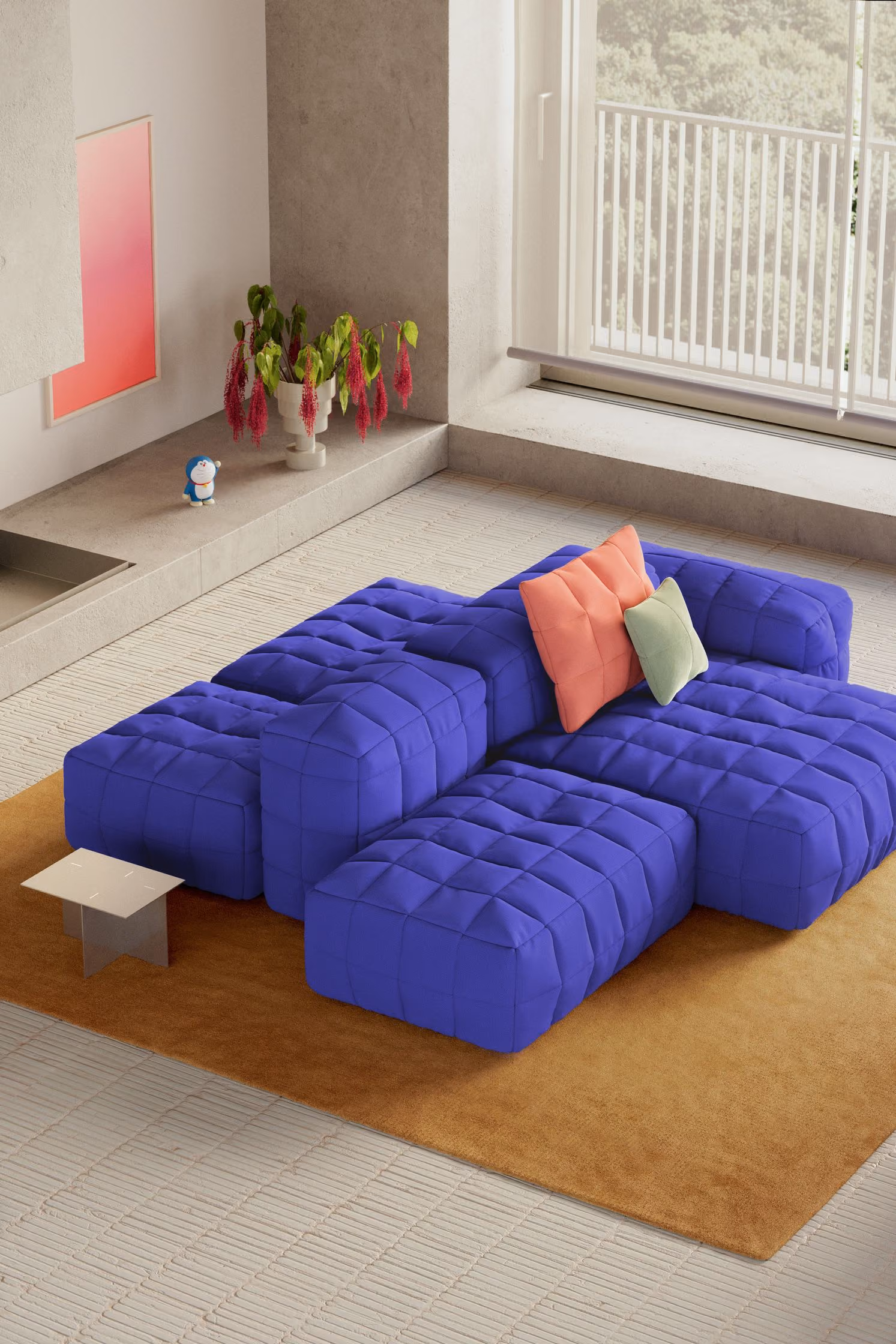 Modern living room with a large, modular royal blue tufted sofa featuring two throw pillows, one coral and one light green, on a brown rug near a large window.