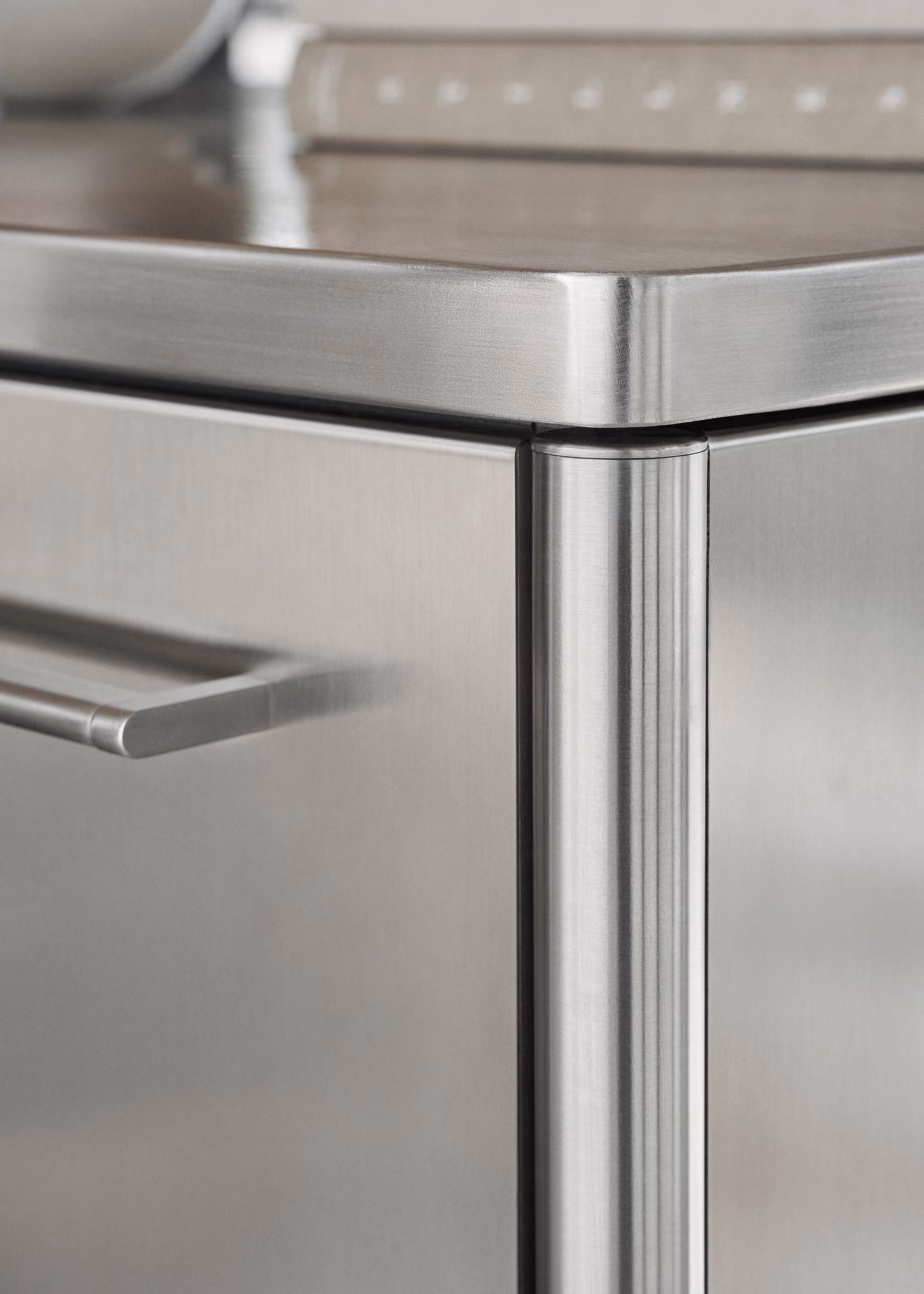 Close-up of a stainless steel kitchen cabinet corner showing the smooth edge, door handle, and part of the countertop surface.