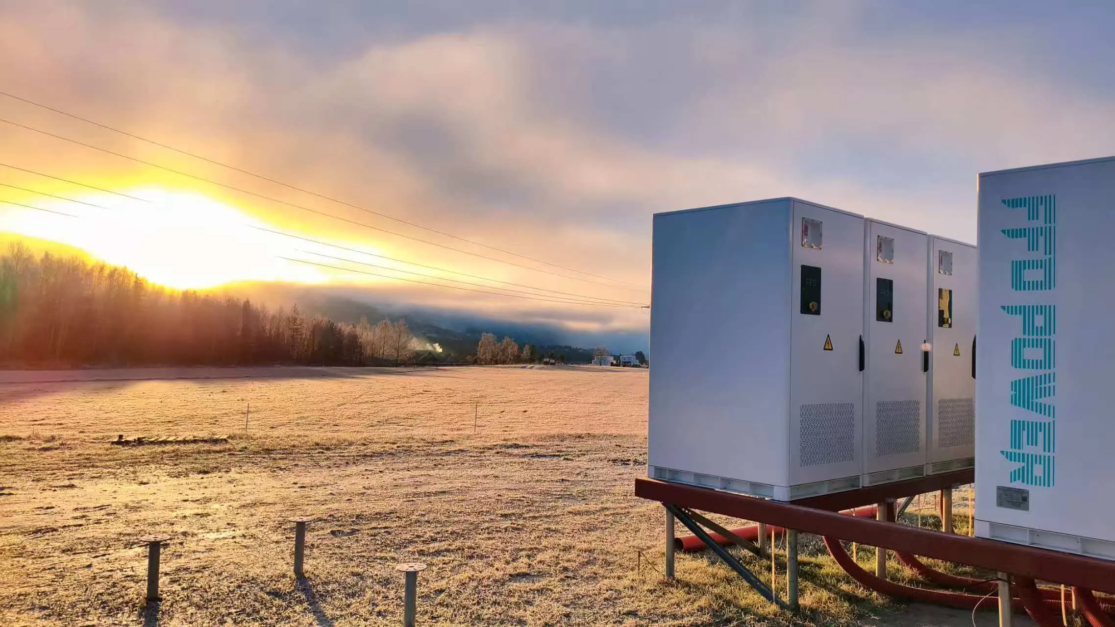FFD POWER Batterieschränke auf einer erhöhten Stahlplattform bei Sonnenaufgang über nebligen norwegischen Feldern