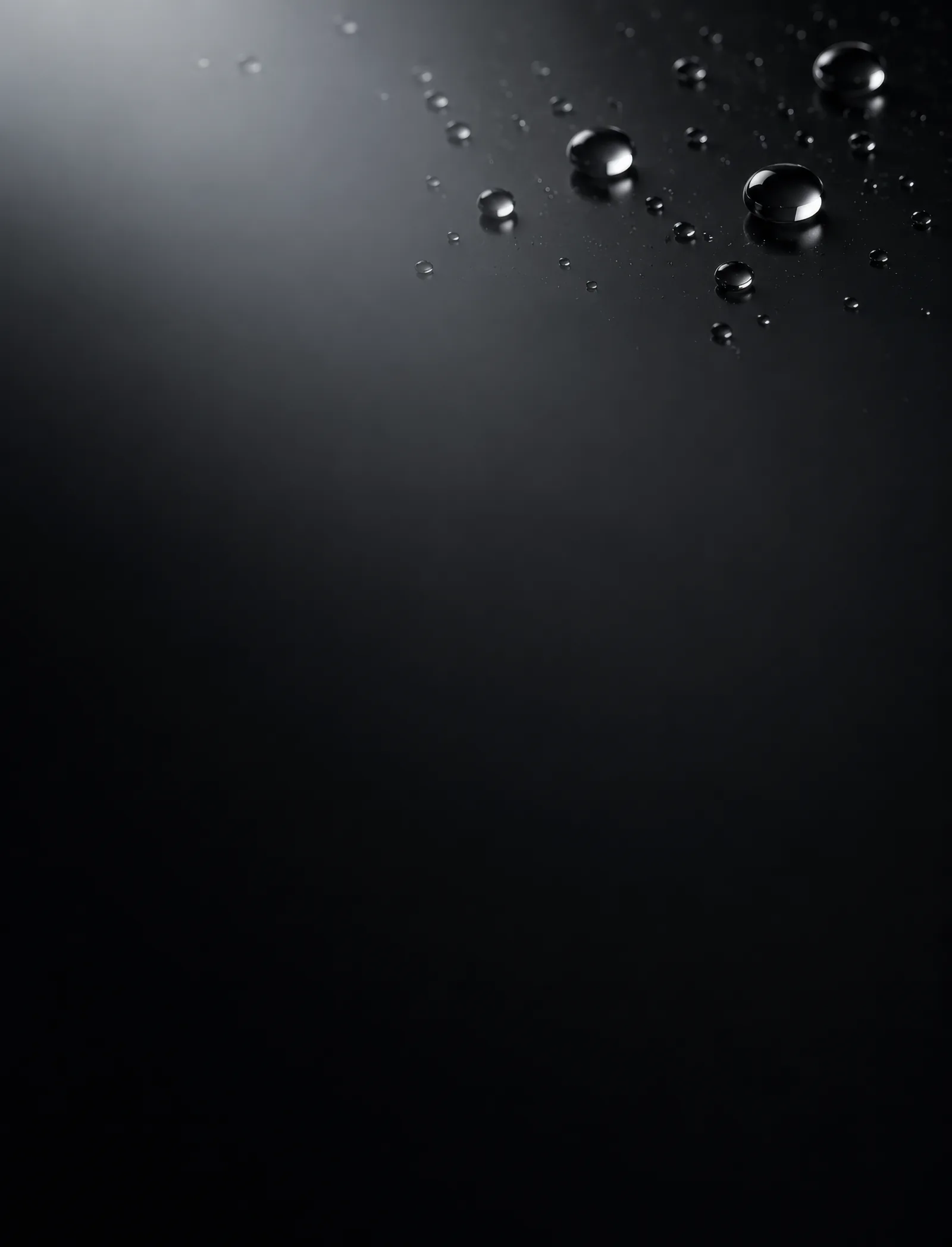 Glossy black surface with scattered water droplets of varying sizes reflecting light.