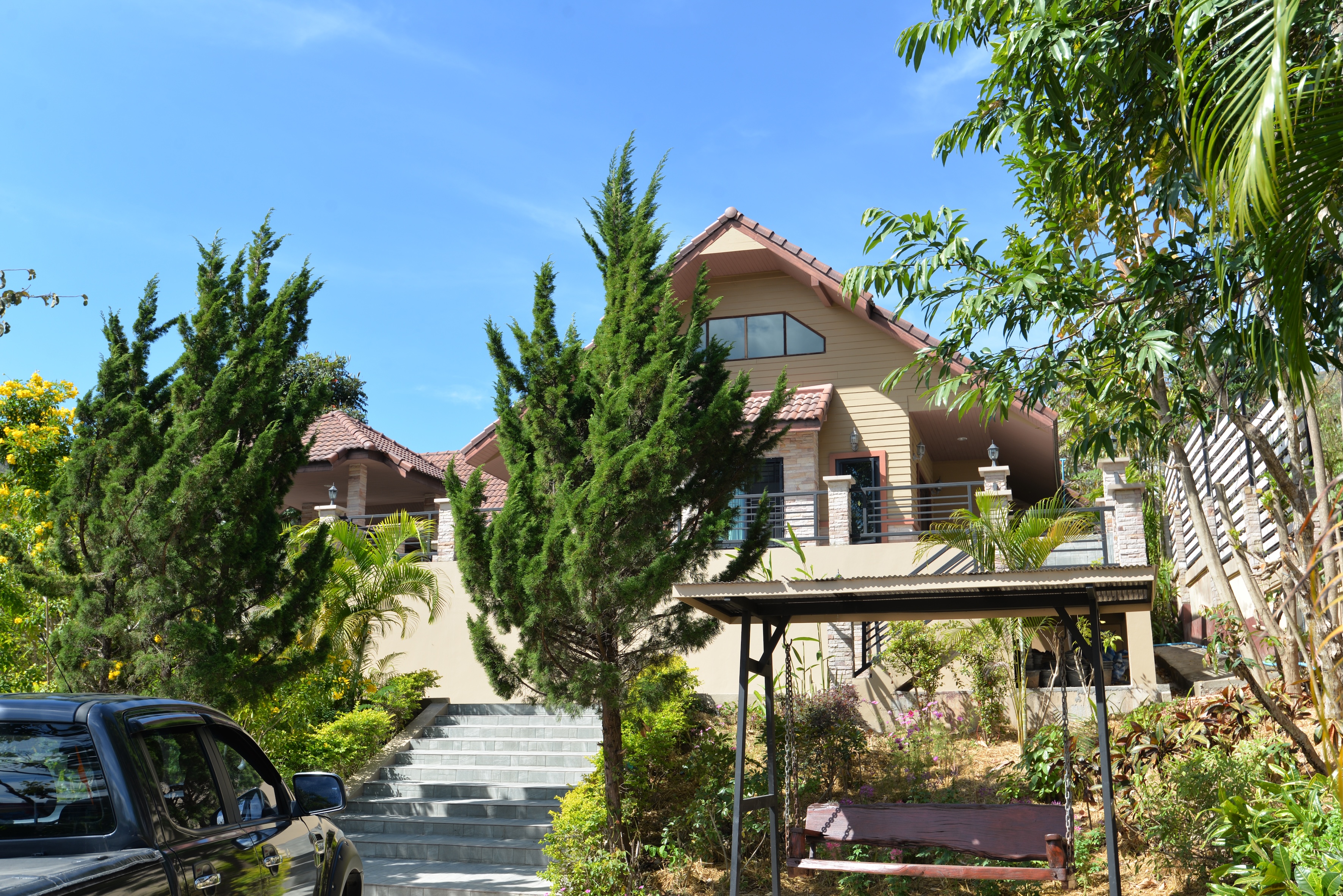 Exterior of Verryn Khao Kho, a private two-story villa surrounded by trees and greenery under a clear blue sky.