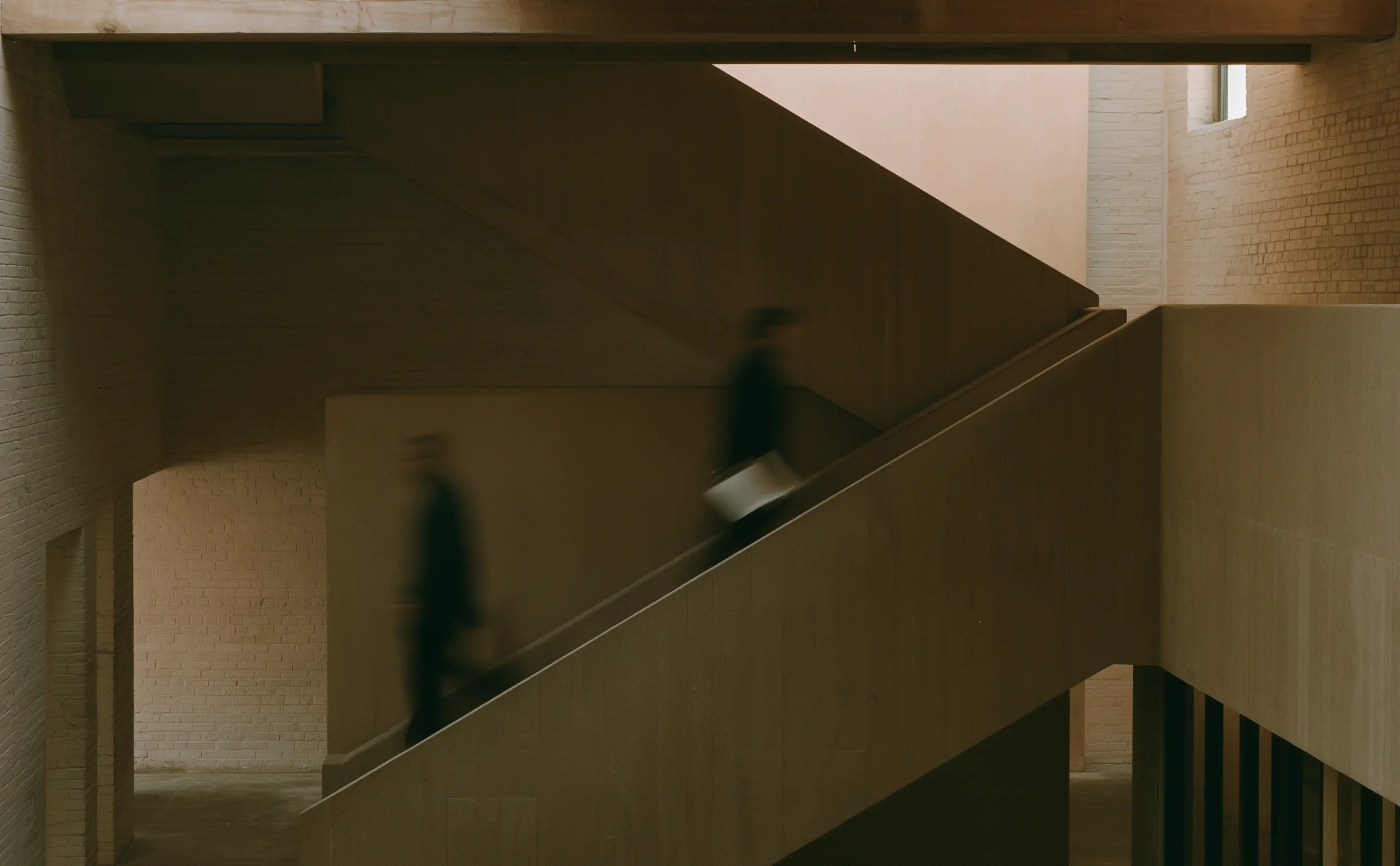 Motion-blurred workers moving through a stark concrete stairwell.