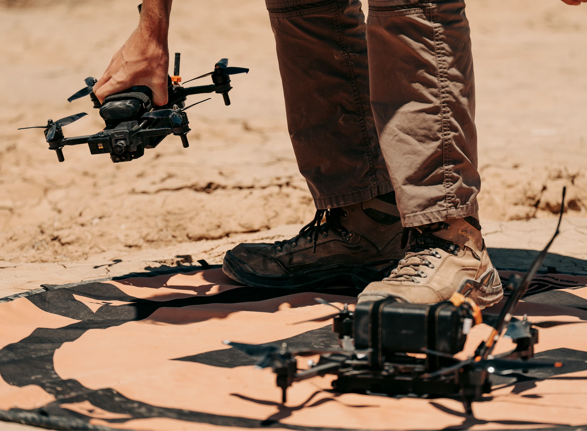 Man holding Neros Archer drone behind second Neros Archer drone atop drone landing pad in desert. 