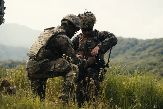 Two soldiers kneeling in grassy field, preparing Neros Archer drone for field training.