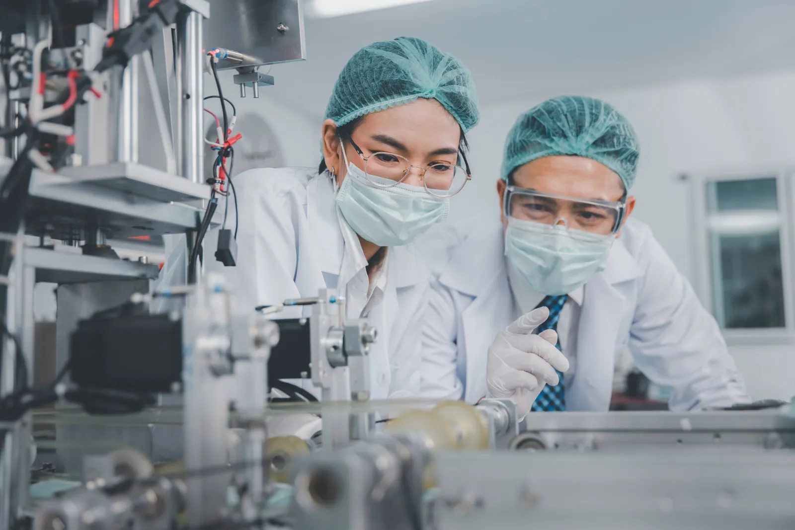 Two scientists in protective gear reviewing work at a pharmaceutical lab bench