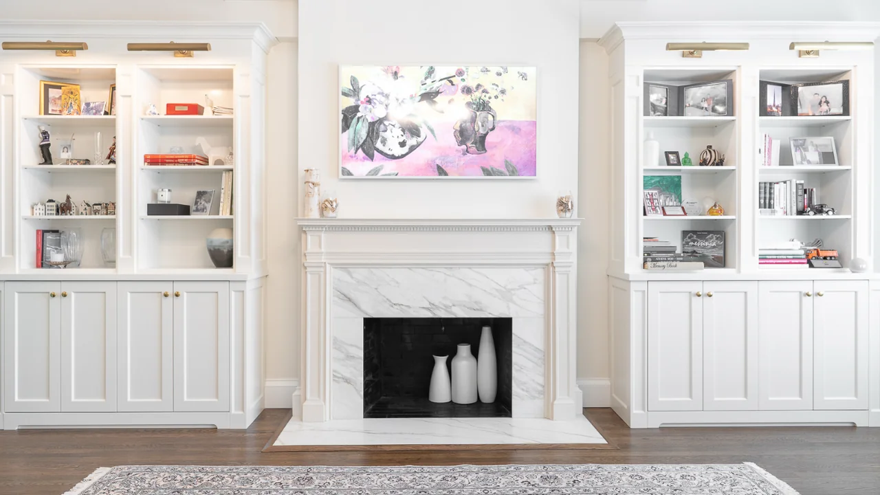 White custom built-in bookshelves and cabinets framing a marble fireplace in a Manhattan apartment.