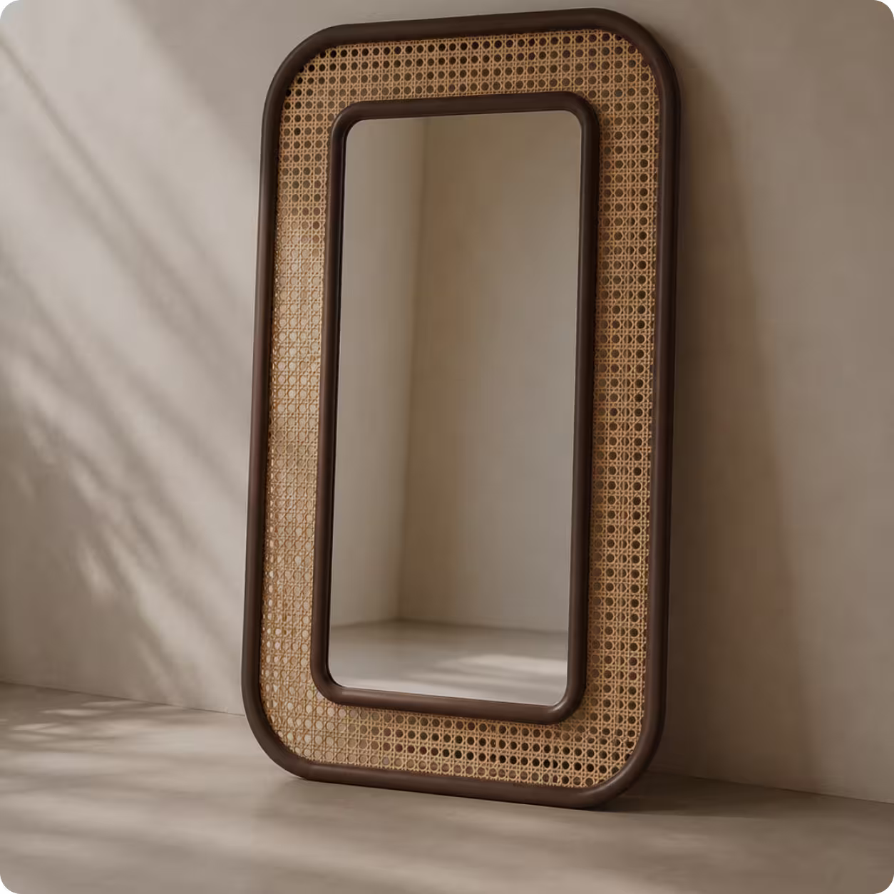 Rectangular mirror with rounded corners and woven rattan frame leaning on beige wall.
