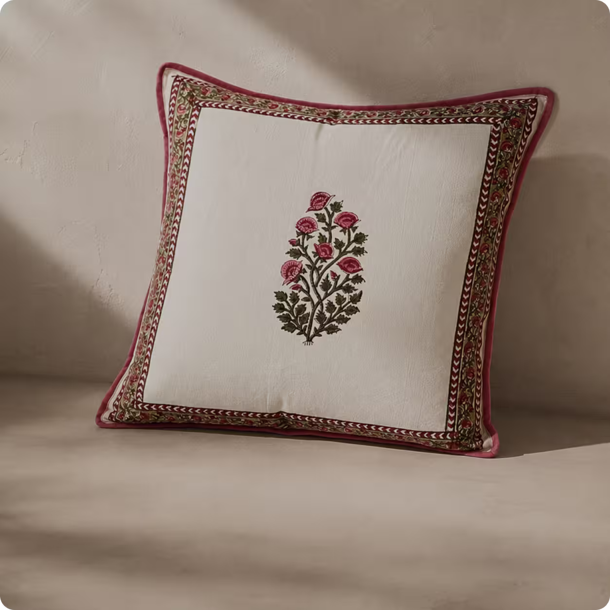 Square white pillow with red and green floral embroidery and decorative border resting on beige surface.
