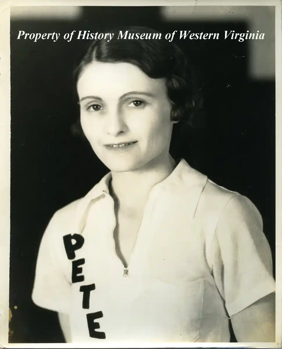 Black and white portrait of a young woman with short dark hair wearing a light-colored collared shirt with the name PETE vertically on the left side, against a dark background.