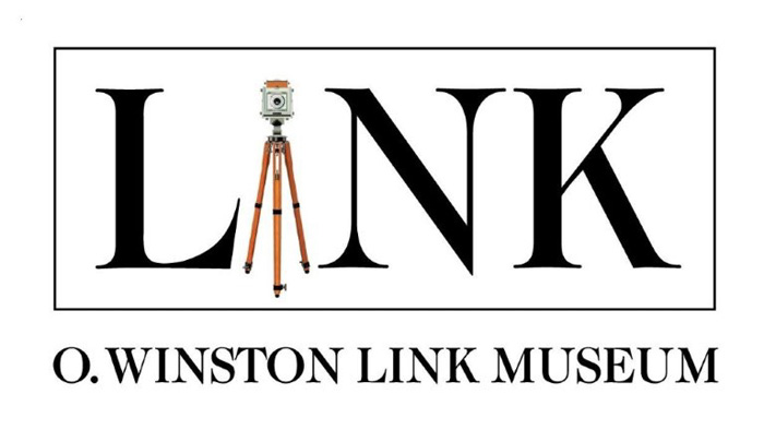 Logo for O. Winston Link Museum featuring the word 'LINK' in large black letters with a vintage camera on a wooden tripod replacing the letter 'I', and 'O. WINSTON LINK MUSEUM' written below in uppercase letters.