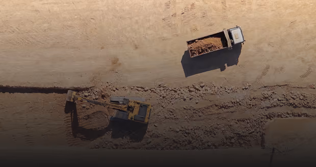 Aerial view of a construction site showing a bulldozer digging and a dump truck filled with dirt on a sandy area.