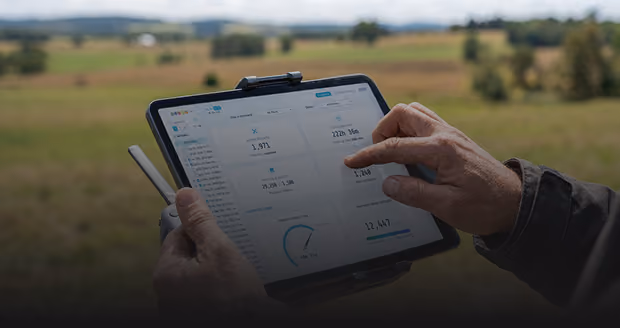 Close-up of hands holding and interacting with a tablet displaying data analytics and performance metrics in a rural outdoor field setting.