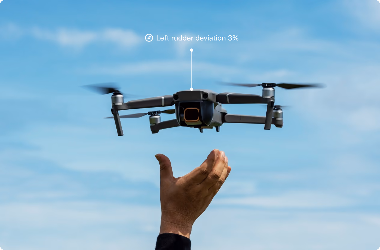 Close-up of a black quadcopter drone with spinning propellers hovering midair above a person's raised hand, with a blue sky background and an overlay text indicating 'Left rutter deviation 3%'.