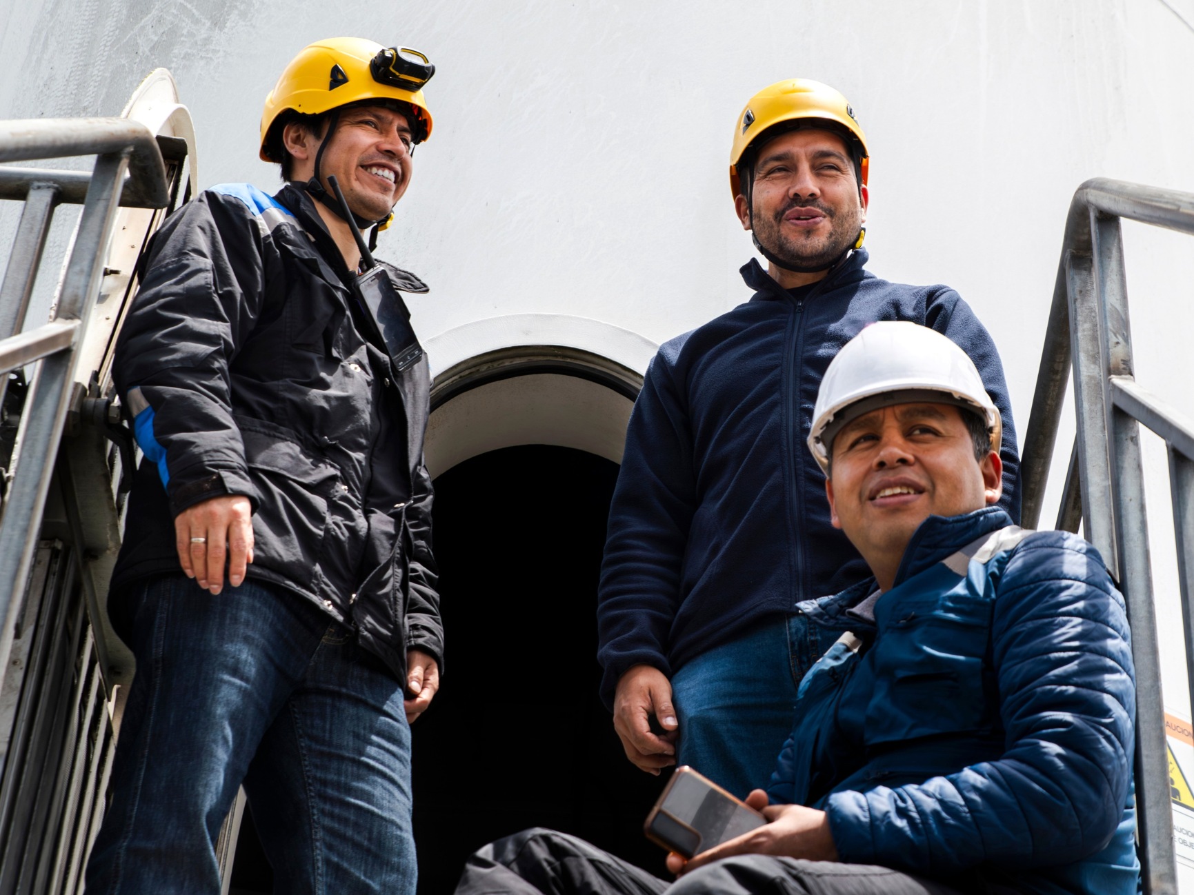 Three workers in hard hats at an industrial site