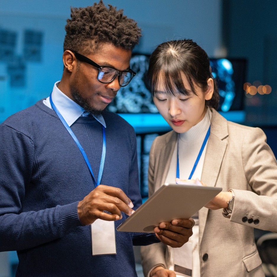 Two colleagues with ID badges reviewing a tablet