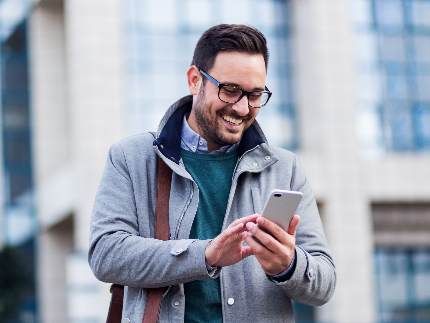 Smiling man in glasses checking his phone outside an office building