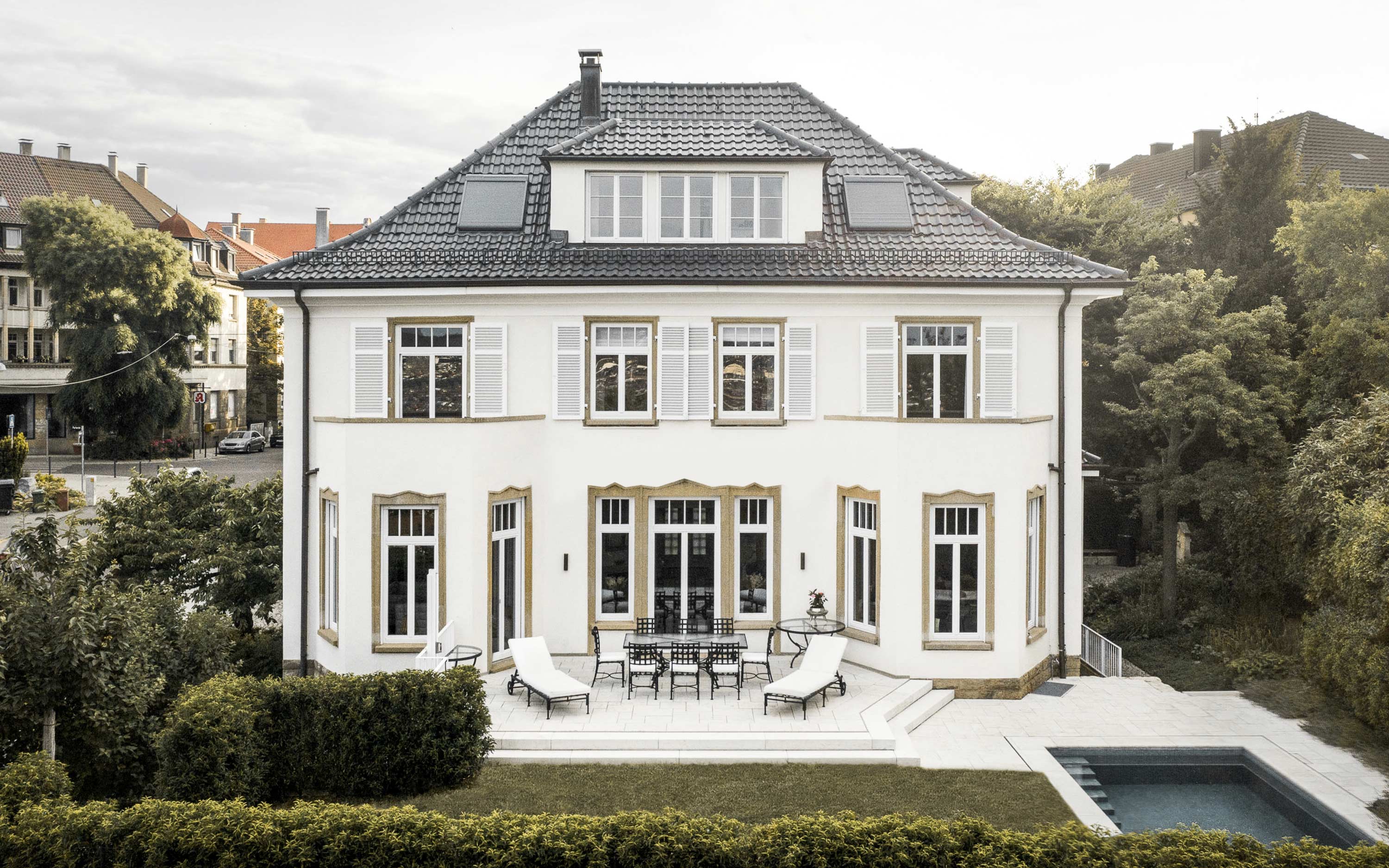 Front view of a classic beige mansion with tall windows, decorative balcony, and dormer windows on roof.