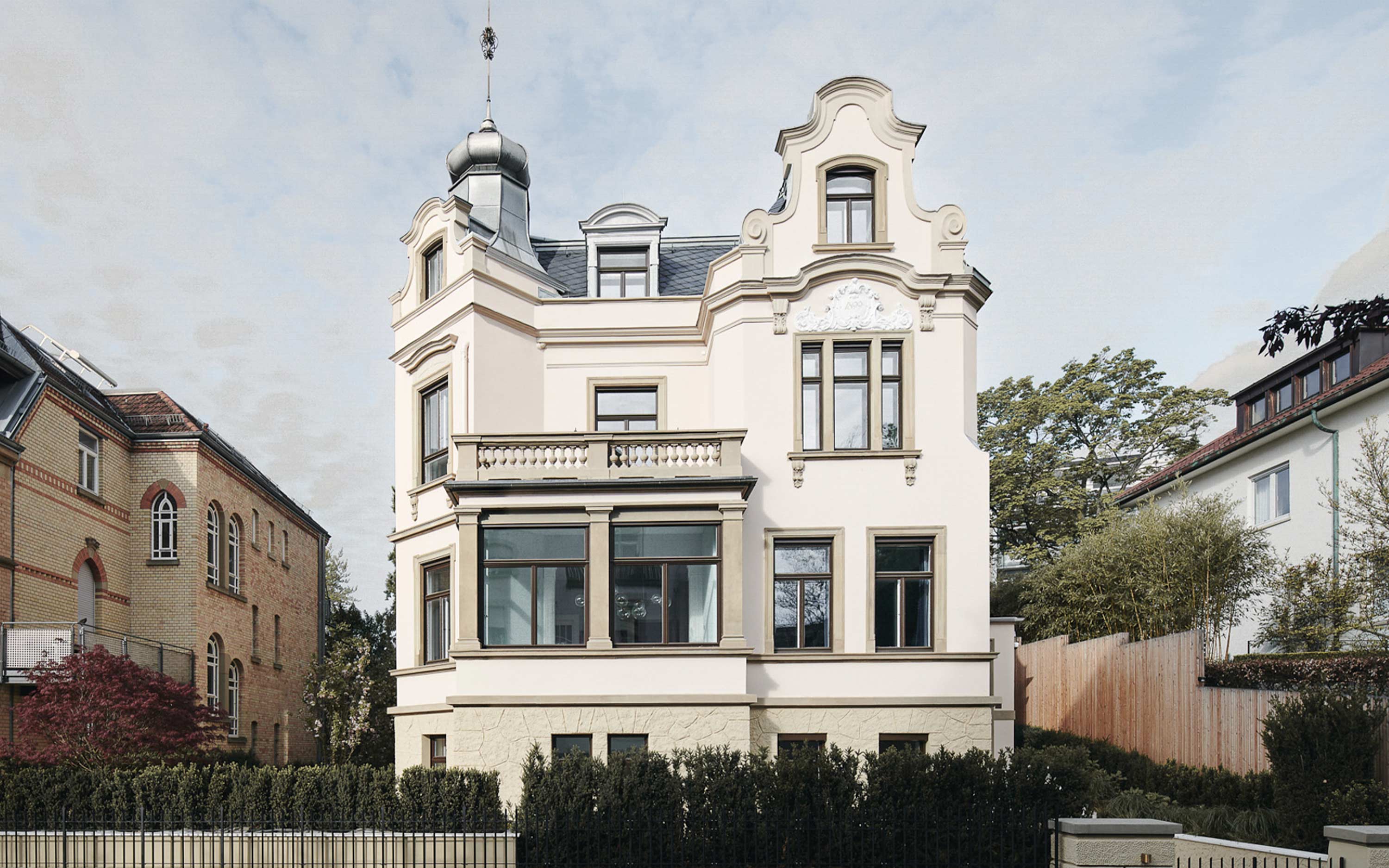 Front view of a classic beige mansion with tall windows, decorative balcony, and dormer windows on roof.