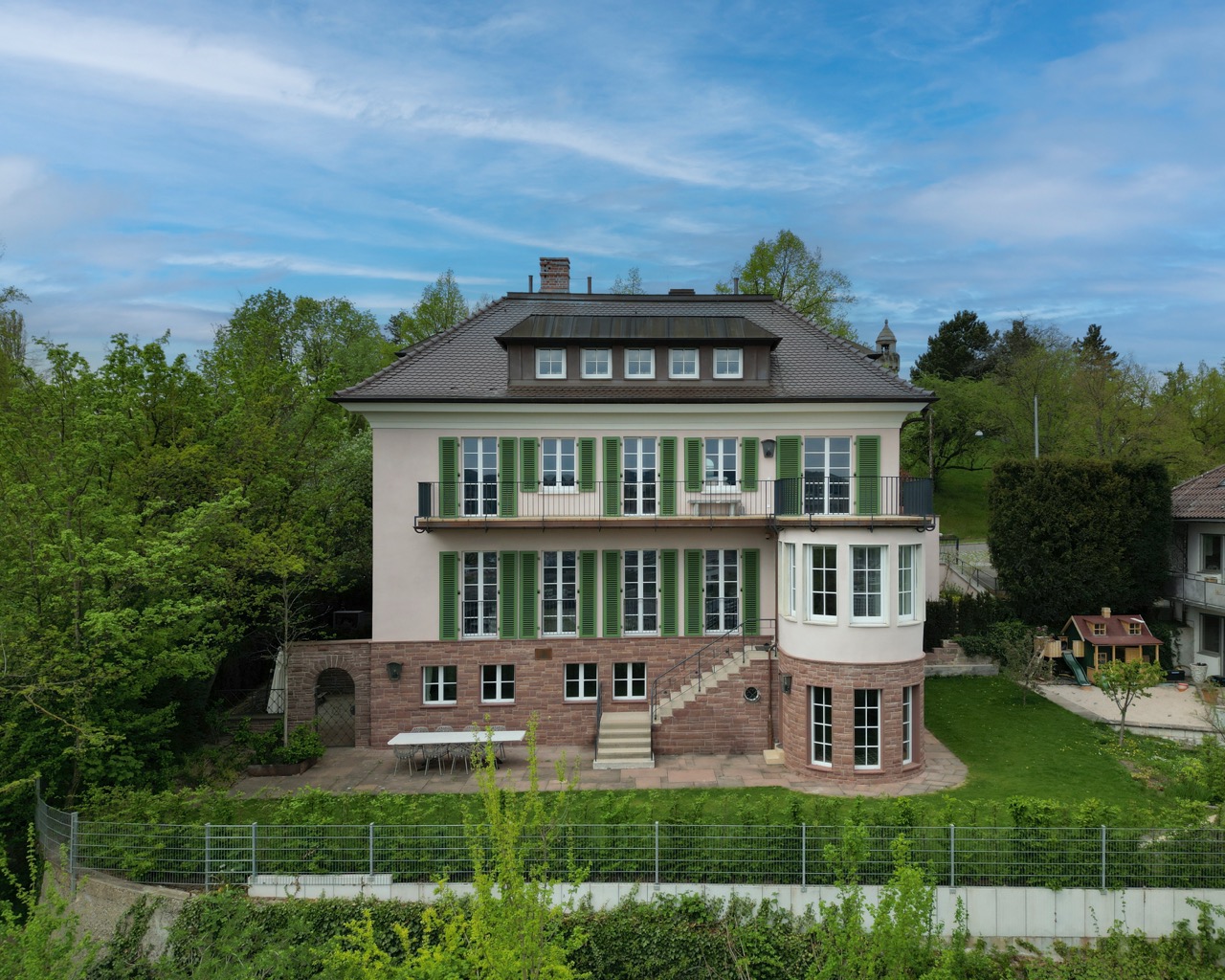 Front view of a classic beige mansion with tall windows, decorative balcony, and dormer windows on roof.