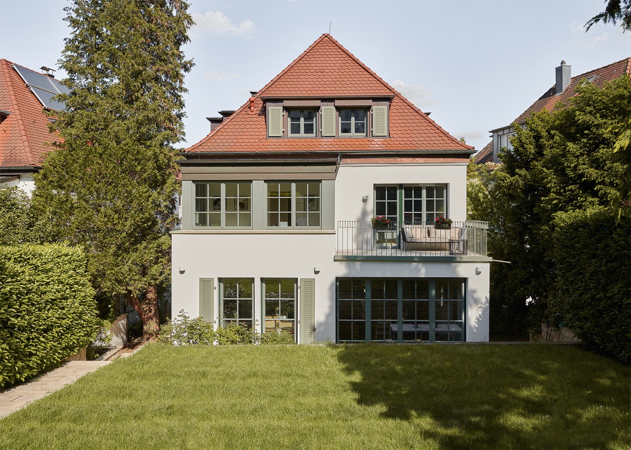 Front view of a classic beige mansion with tall windows, decorative balcony, and dormer windows on roof.
