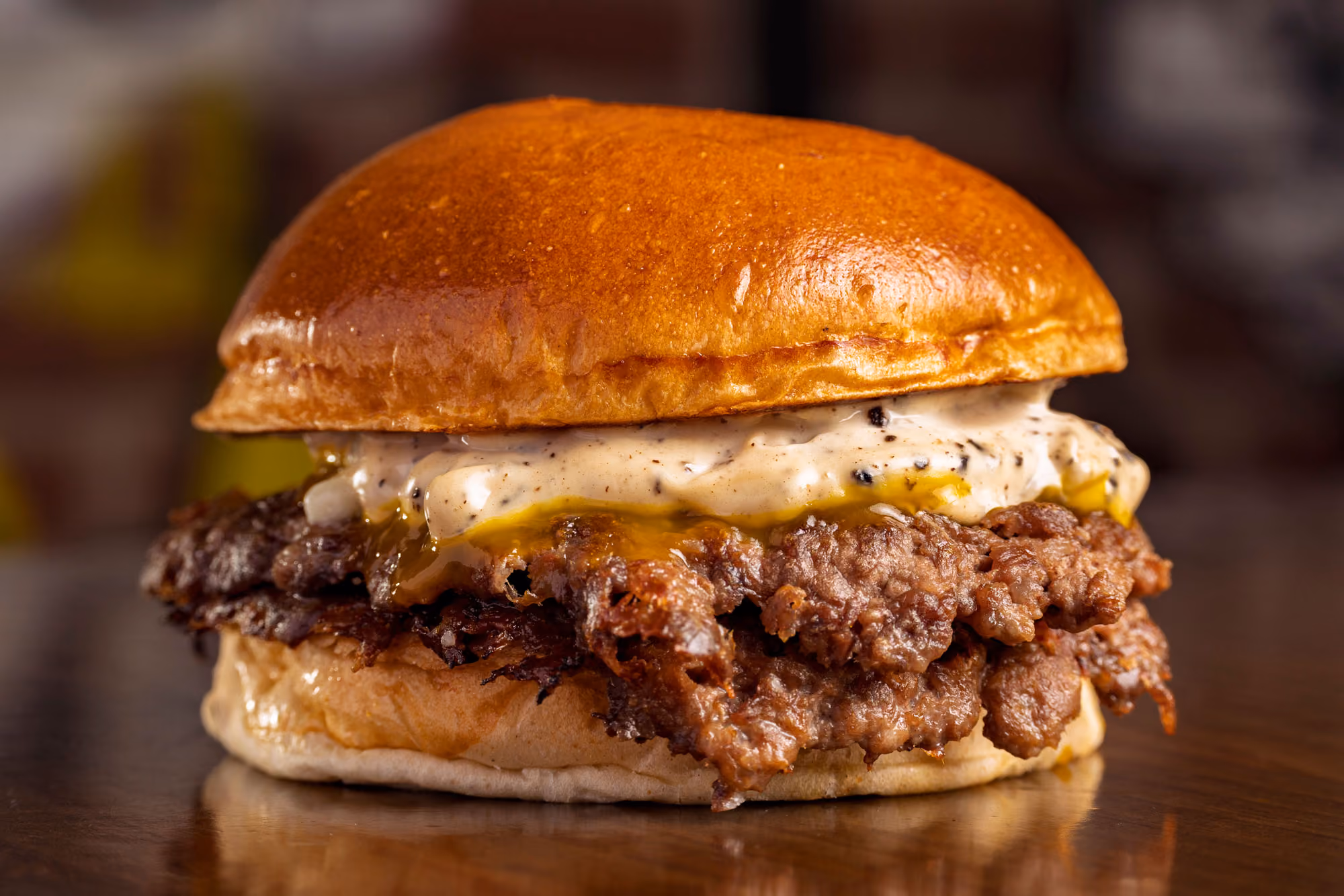 Close-up of a crispy fried chicken sandwich with creamy sauce on a glossy toasted bun.
