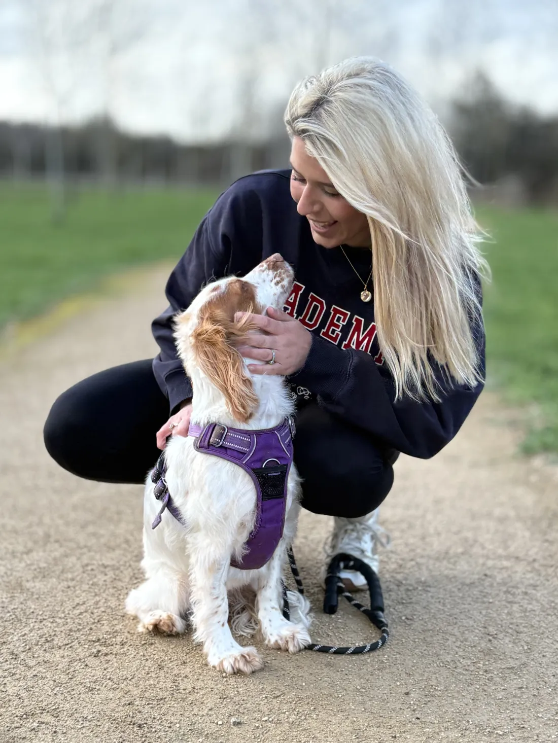 Steph, founder of Prior & Pooch, crouching on a countryside path with her orange roan working cocker spaniel, Willow