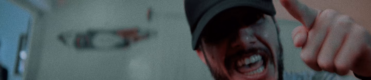 Hombre con gorra negra señalando hacia la cámara con expresión intensa y boca abierta.