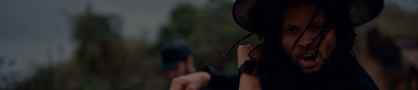 Primer plano de hombre con sombrero oscuro haciendo un gesto enérgico al aire libre.