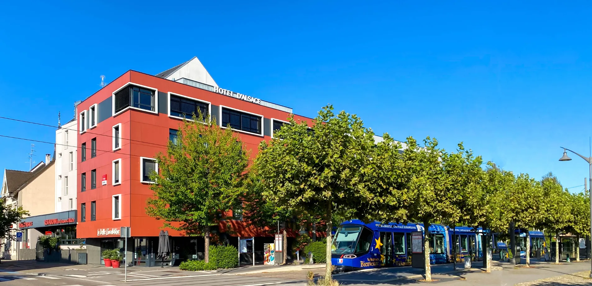Enseigne Hôtel d'Alsace sur sa façade rouge bordée d'arbres, à deux pas de l'arrêt de tram vers Strasbourg