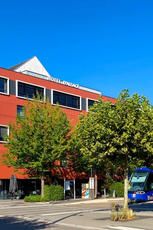 Enseigne Hôtel d'Alsace sur sa façade rouge bordée d'arbres, à deux pas de l'arrêt de tram vers Strasbourg