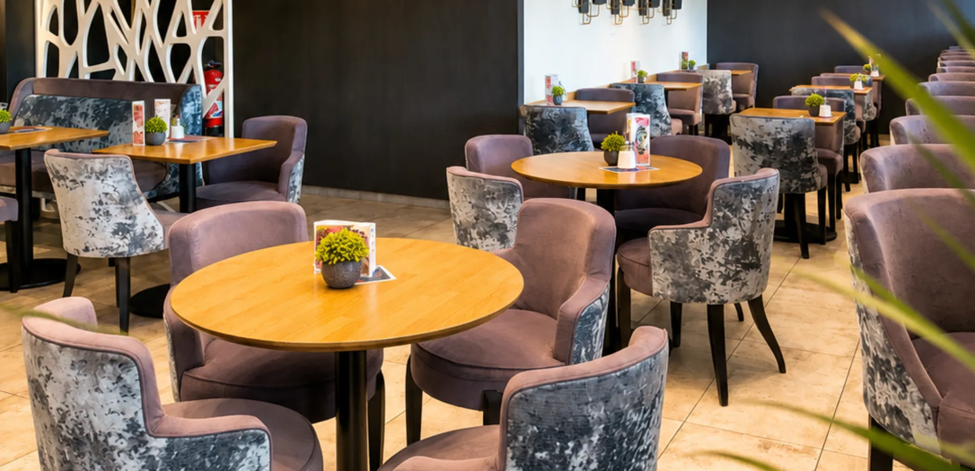 Salon aux fauteuils en velours gris et tables rondes en bois de l'Hôtel d'Alsace, à Illkirch près de Strasbourg