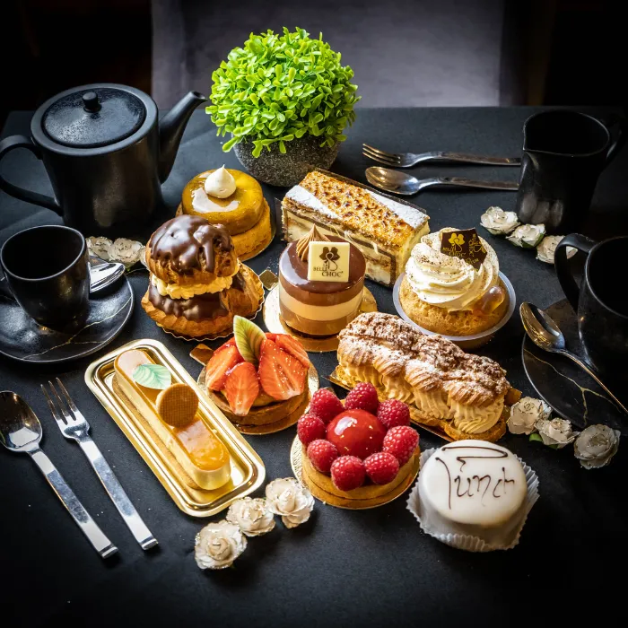 Assortiment de pâtisseries françaises sur une table noire : religieuse, mille-feuille, paris-brest, tartes aux fruits rouges, accompagnées d'un service à thé
