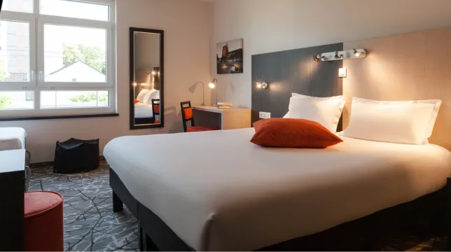 Chambre chaleureuse avec grand lit, liseuses murales, poufs colorés et miroir mural