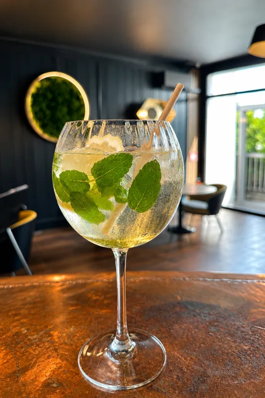 Cocktail pétillant à la menthe fraîche et au citron dans un verre ballon, posé sur un comptoir cuivré