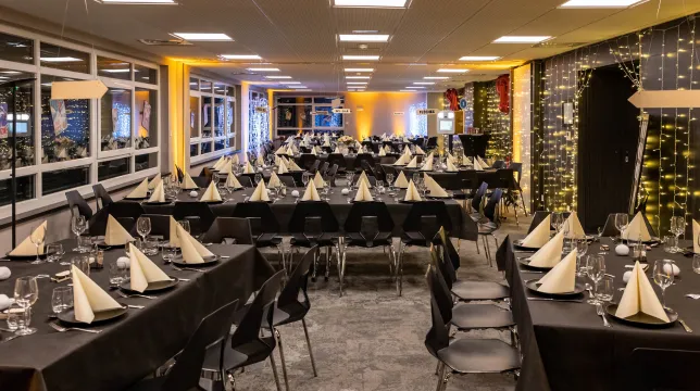 Grande salle de réception dressée pour un banquet avec nappes noires, serviettes dorées et guirlandes lumineuses à l'Hôtel d'Alsace