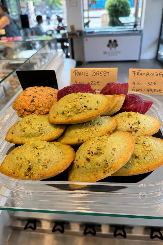 Gros plan sur des madeleines parsemées d'éclats de pistache et un cookie dans la boutique La Belle Choc'