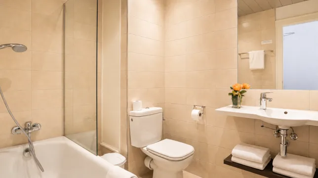 Salle de bain avec baignoire, toilettes et petit bouquet de roses orangées près du lavabo à l'Hôtel d'Alsace