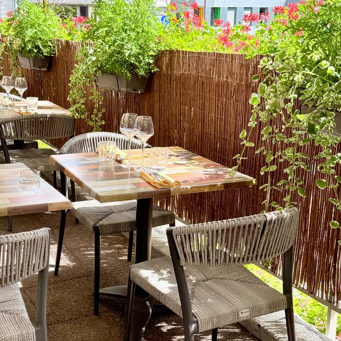 Terrasse fleurie du restaurant Les Terrasses d'Illkirch avec tables en bois coloré et chaises en corde tressée à l'Hôtel d'Alsace