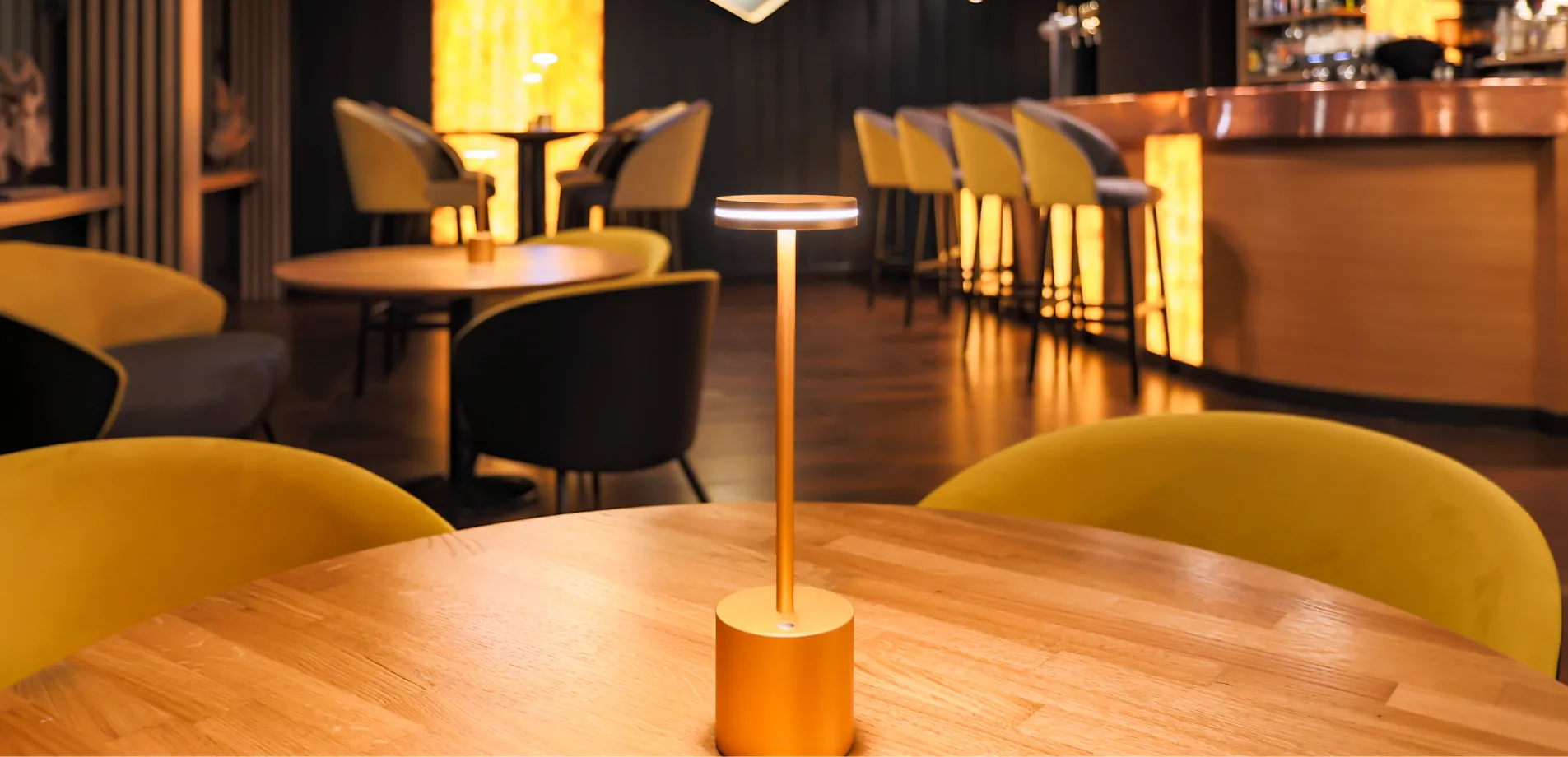 Ambiance tamisée du bar L'ill'ixir avec tabourets jaunes et lampe de table dorée à l'Hôtel d'Alsace