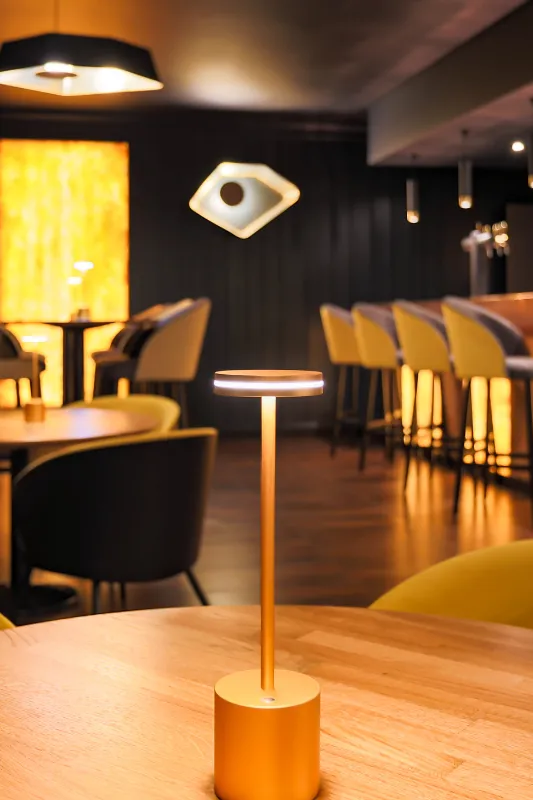 Ambiance tamisée du bar L'ill'ixir avec tabourets jaunes et lampe de table dorée à l'Hôtel d'Alsace