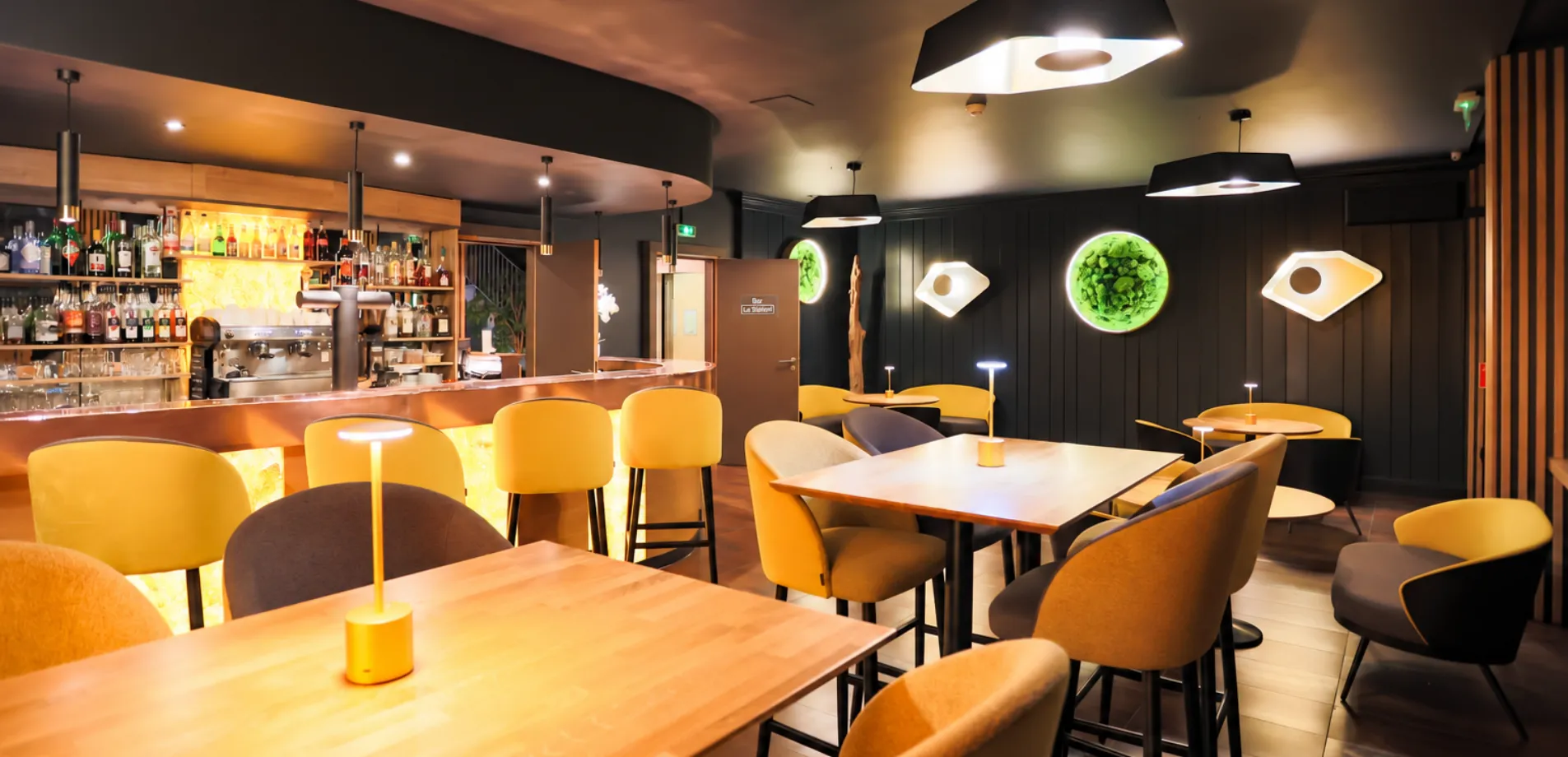 Bar de l'hôtel à Illkirch aux fauteuils jaunes, tables en bois et comptoir éclairé, près de Strasbourg