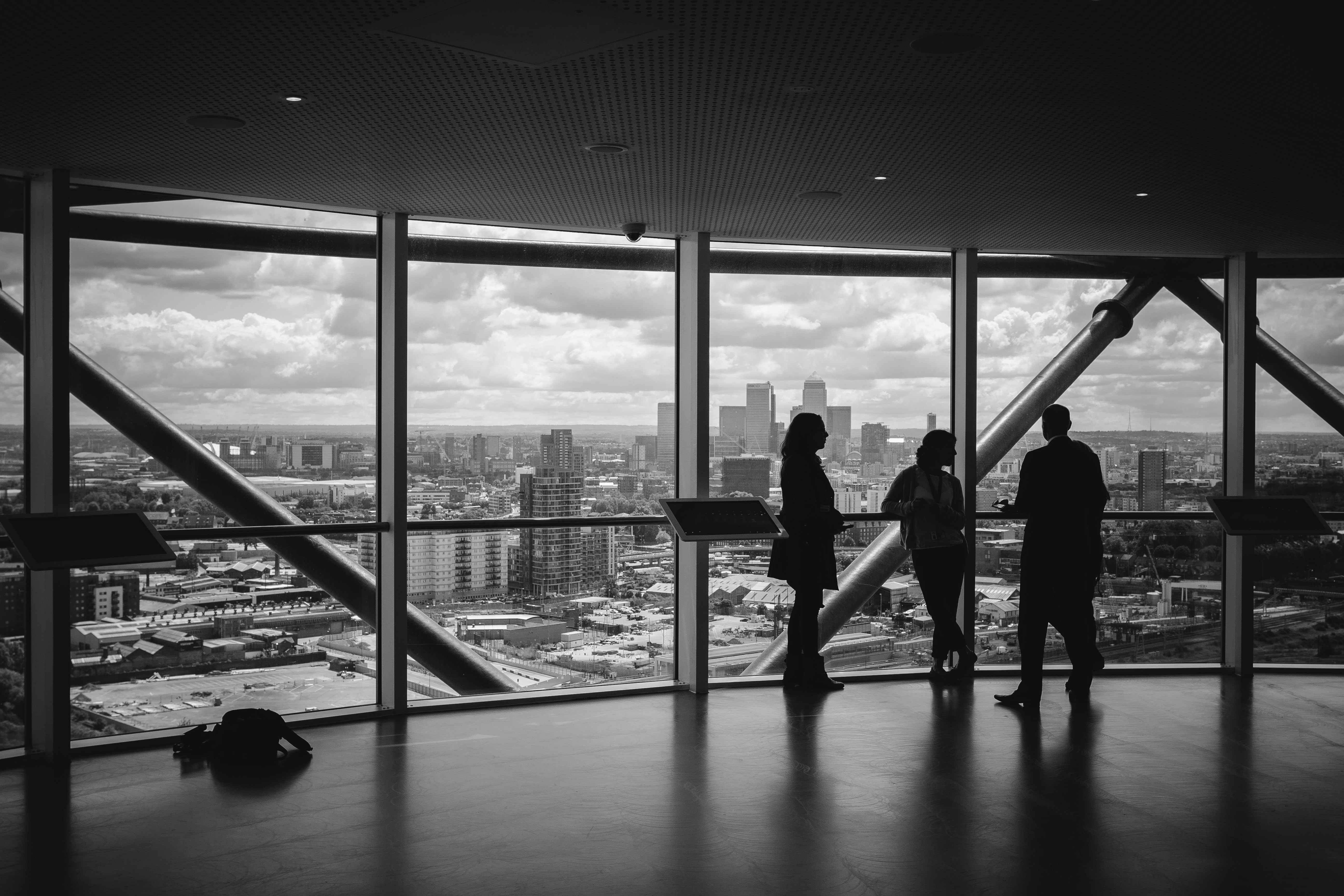 Silhouettes of three people inside a building with large windows overlooking a cityscape.