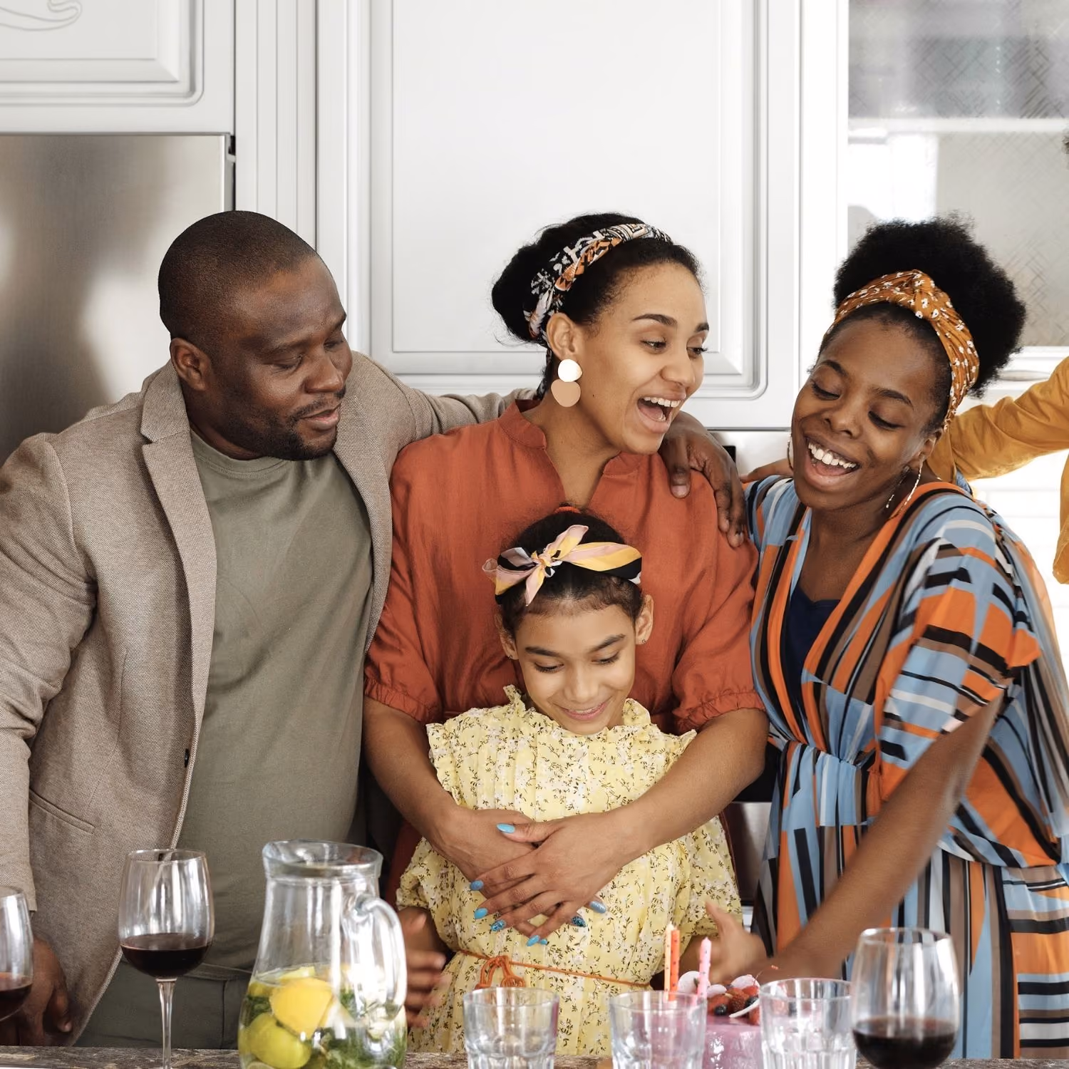 Smiling family hugging and celebrating around a table with drinks in a kitchen.