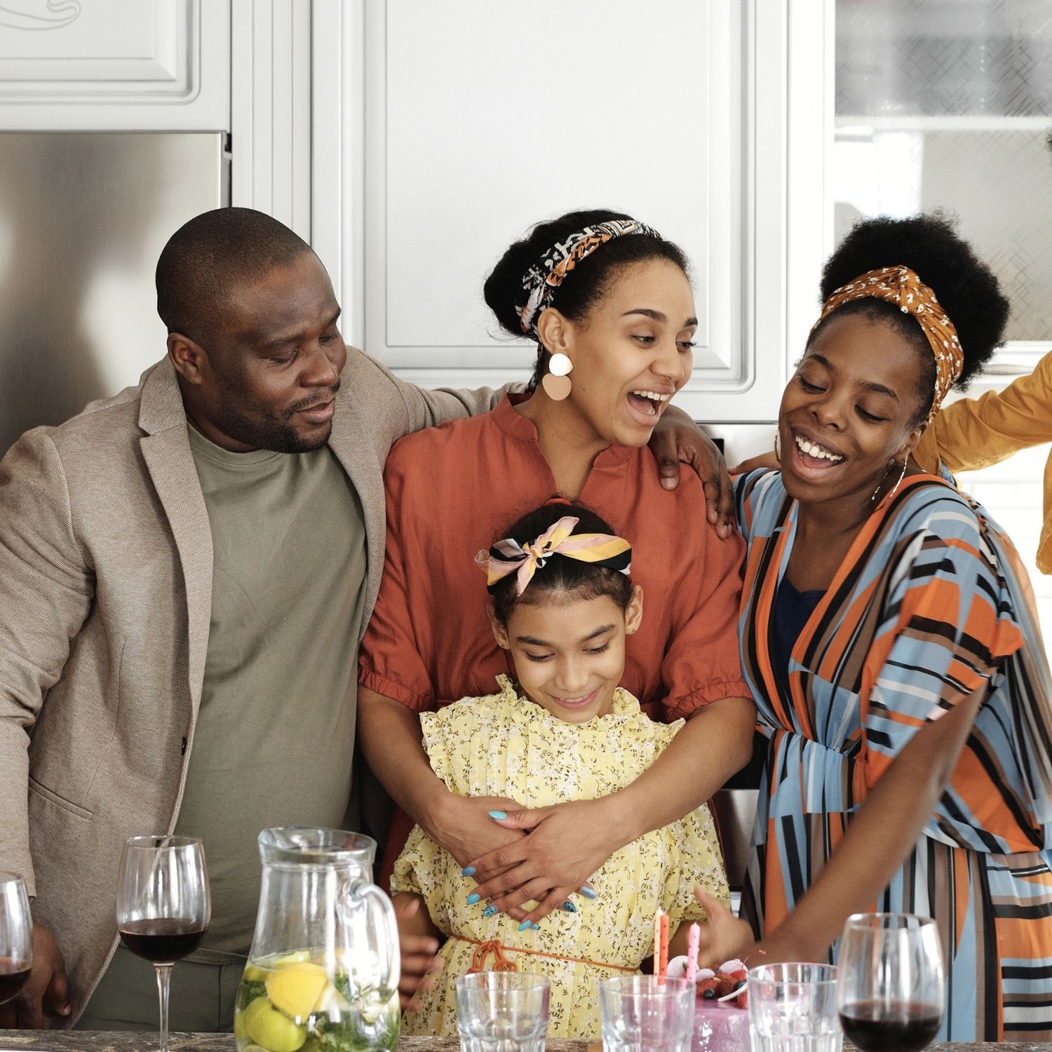Smiling family hugging and celebrating around a table with drinks in a kitchen.