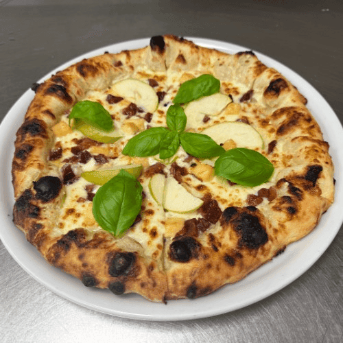 Freshly baked pizza with basil leaves and apple slices on a white plate.