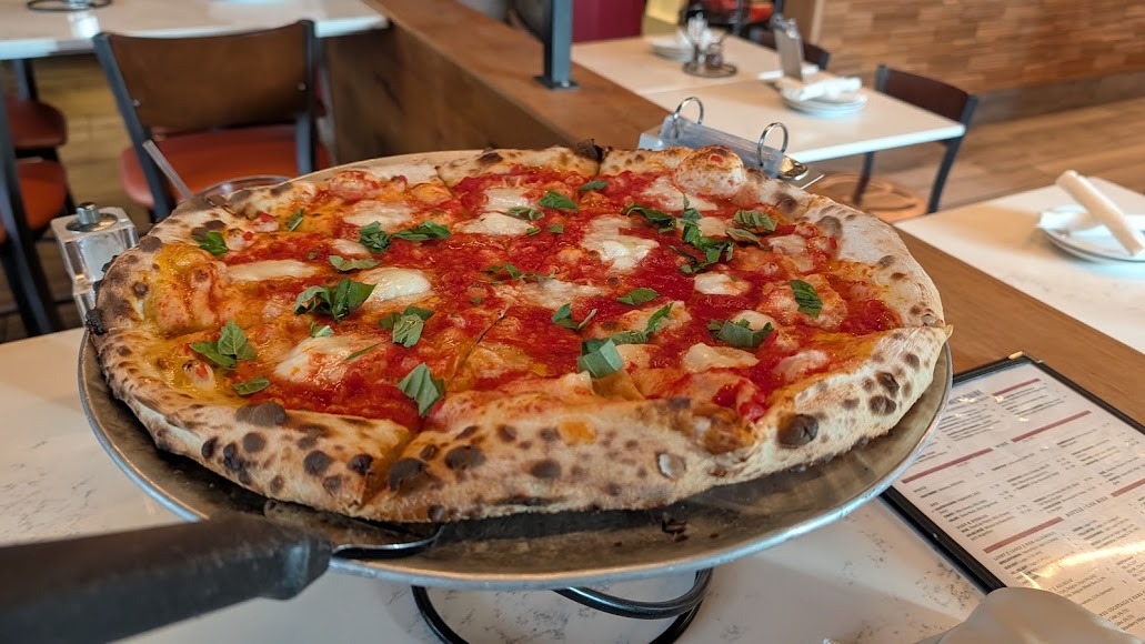 Freshly baked Margherita pizza with tomato, mozzarella, and basil served on a raised metal tray.